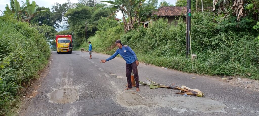 Warga Desa Sukalilah Kecamatan Cibatu menambal lubang di jalan kabupaten dengan semen